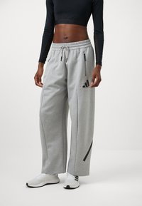Pantaloni sportivi grigi con vita elasticizzata, tasche laterali con zip e un logo nero sulla coscia. Materiale morbido e design a gamba ampia.