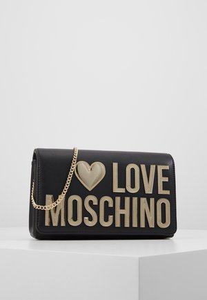 Pochette Black Love Moschino avec grand cœur beige et lettrage, avec une chaîne dorée, exposée sur un piédestal blanc.
