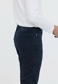 Jeans de mezclilla azul oscuro con un diseño ajustado, que presentan un detalle de costura contrastante en el bolsillo trasero y una etiqueta de marca de cuero en la cintura.