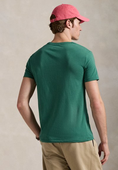 Zaļš kokvilnas t-krekls ar apaļu kakla izgriezumu un īsām piedurknēm, ar mīkstu tekstūru. Kombinēts ar gaiši rozā cepuri.