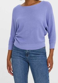 Pull ample couleur lavande avec encolure bateau, manches 3/4 et design côtelé texturé, associé à un jean bleu ajusté.