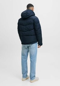 Chaqueta acolchada navy con capucha, con un diseño acolchado y puños elásticos. Combinada con jeans rectos de color azul claro y zapatillas.