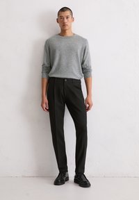 Un pull en laine gris à col rond, un pantalon noir élégant et des chaussures en cuir noires. La tenue présente un design simple et moderne avec une silhouette ajustée.