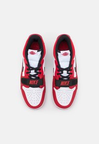 Červené a bílé tenisky s černými akcenty, s polstrovaným límcem, perforovanou špičkou a výrazným černým pásem s nápisem "NIKE."