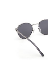 Runde Sonnenbrillen mit dunkelgrauen Gläsern, dünnem silbernem Metallrahmen, klaren Nasenpads und verjüngten grauen Bügeln. Minimalistisches Design.