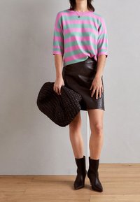 Pull rayé rose et vert, mini-jupe en cuir, sac à main noir texturé, et bottines, avec un bout pointu et un design élégant.
