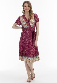 Rochie tip wrap de un magenta profund, cu modele florale, mâneci scurte și o curea modelată; prezintă o bandă contrastantă la tiv.