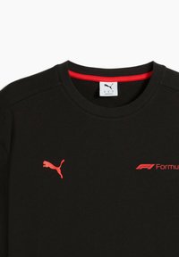 Sort T-shirt med et rødt Puma-logo og "Formula 1" branding på forsiden, samt en rød indvendig krave.