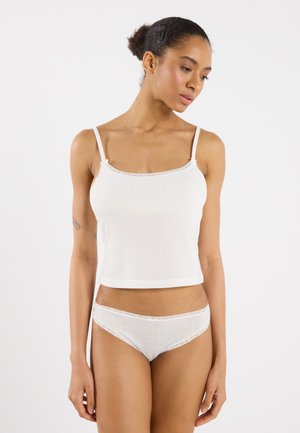 Witte geribde tanktop met verstelbare bandjes en kantafwerking, gecombineerd met bijpassende witte slip met kantaccenten en een textuurpatroon.