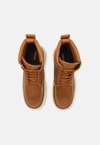 Hnědé kožené boty s kulatou špičkou, oranžovými tkaničkami a krémovou podrážkou. Mají prošívané detaily a poutko na límci.