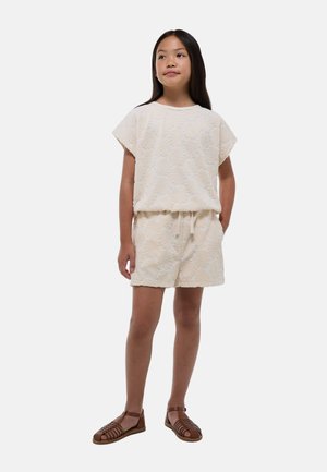 Tenue texturée de couleur claire comprenant un haut ample et un short à taille élastique, tous deux ornés d'un motif de coquillage. Associée à des sandales brunes à lanières.