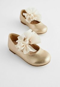 Guldsyntetiska läderballetskor med rund tå, prydda med en stor krämfärgad chiffonblomma på framfoten.