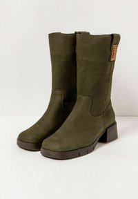Botas de tobillo de ante sintético verde con punta cuadrada, tacón bloque y cremallera lateral; presentan un diseño cosido y una etiqueta decorativa.