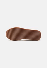 Suela de goma marrón con estrías verticales, bordes curvados y una textura suave. El diseño es ligero y flexible.