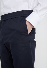 Granatowe spodnie z elastycznym paskiem w talii, z bocznymi kieszeniami, gładką fakturą i szczegółowym przeszyciem, zestawione z elegancką białą koszulą z guzikami.