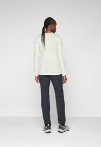 Haut à manches longues léger de couleur beige clair associé à un pantalon gris foncé et des baskets noires et violettes, présentant un design simple et une coupe ajustée.