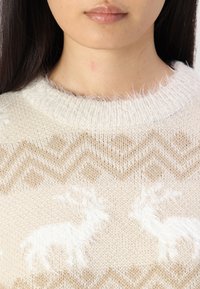 Witte en beige gebreide trui met een textuurpatroon, voorzien van rendiermotieven en een zigzagontwerp, afgewerkt met een donsachtige kraag.