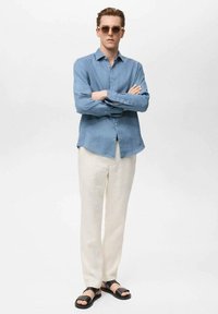 Blue linen button-up shirt, cream-colored linen trousers, and black sandals. The shirt has a relaxed fit and long sleeves.