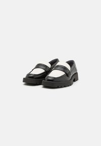 Black and white slip-on shoes with a textured leather upper, featuring contrasting elastic straps and a chunky treaded sole.