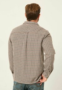 Braun- und cremefarbener Hahnentrittmuster-Hemd mit Button-Down-Kragen, langen Ärmeln und Rückenpassform, getragen über blauen Jeans.