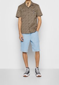 Košile s krátkým rukávem v leopardím vzoru se dvěma kapsami na prsou, spárovaná se světle modrými džínovými šortkami a černými vysokými teniskami s bílými tkaničkami.