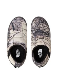 Scarpe slip-on texture, isolate per interni/esterni, di colore beige chiaro con motivo di rami neri. Presentano un logo e un morbido rivestimento nero.