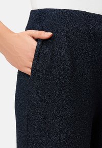 Ciemnoniebieskie spodnie z teksturowanej tkaniny o subtelnym połysku. Zawierają boczną kieszeń oraz dopasowany pas.
