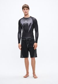 Czarna koszulka do pływania z długim rękawem z szarymi akcentami i wzorzystym przodem, zestawiona z czarnymi szortami kąpielowymi z kontrastowym przeszyciem i sznurkiem.