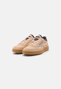 Beige leather sneakers with a white accent stripe, perforations on the toe, and a gum rubber sole. Includes gray padded collar and laces.