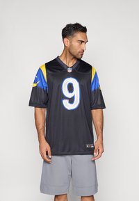 Μαύρη φανέλα NFL με κίτρινα και μπλε στοιχεία, με μεγάλο λευκό αριθμό 9 στο μπροστινό μέρος. Φοριέται με γκρι σορτς, λείο ύφασμα.