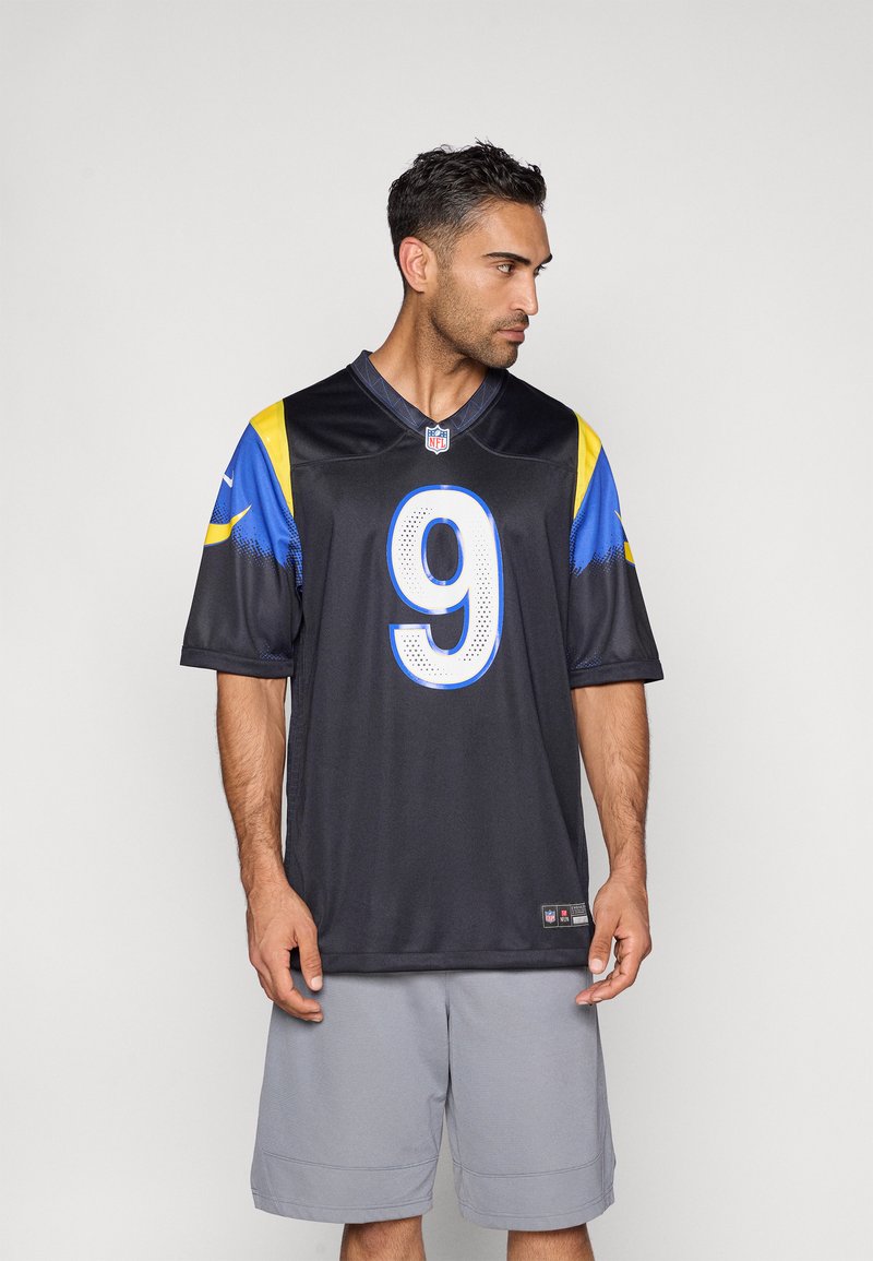 Μαύρη φανέλα NFL με κίτρινα και μπλε στοιχεία, με μεγάλο λευκό αριθμό 9 στο μπροστινό μέρος. Φοριέται με γκρι σορτς, λείο ύφασμα.