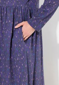 Abito viola con una trama decorata che presenta motivi rosa e blu. Maniche lunghe e vita elastica con tasche laterali.