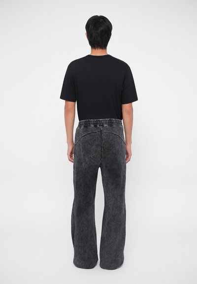 Graue, ausgestellte Hose mit strukturierter Oberfläche, ausgestattet mit einem elastischen Bund und einem schlichten schwarzen T-Shirt. Rückansicht ohne sichtbare Muster.