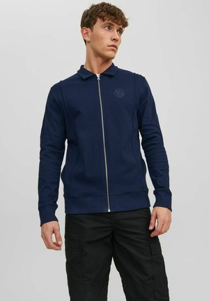 Veste zippée marine avec un col, des manches longues et un détail de logo ; faite d'un tissu lisse avec des poignets et un ourlet côtelés.