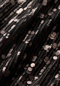 Tela negra con lentejuelas redondas brillantes de diferentes tamaños cosidas en patrones lineales, creando textura e interés visual.