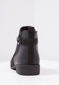 Botín negro hasta el tobillo con cuero texturizado en patrón de reptil y suaves acentos de ante, con un bajo tacón cuadrado y un detalle elástico en el lateral.