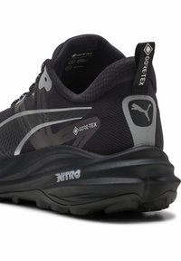 Scarpa da corsa nera con tomaia testurizzata, marchio GORE-TEX, dettagli riflettenti, suola ammortizzata e un'etichetta NITRO ben visibile sul tallone.
