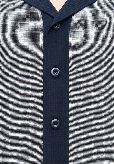 Gros plan d'un cardigan bleu marine boutonné avec un tissu à rayures horizontales blanches et bleu marine de chaque côté.