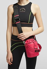 Top corto nero con accenti verde fluo e arancione, abbinato a una piccola borsa a secchiello rotonda in pelle rosa con chiusura a coulisse.