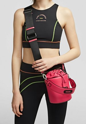 Top corto nero con accenti verde fluo e arancione, abbinato a una piccola borsa a secchiello rotonda in pelle rosa con chiusura a coulisse.