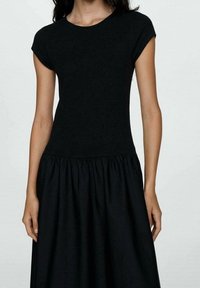 Robe noire avec un corsage ajusté à manches courtes et une jupe évasée et plissée. Fabriquée à partir d'un tissu lisse et léger.