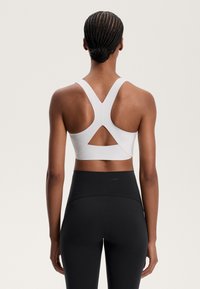 Weißer Sport-BH mit Kreuzträger-Design und weicher Textur, kombiniert mit hochgeschnittenen schwarzen Leggings mit glatter Oberfläche.
