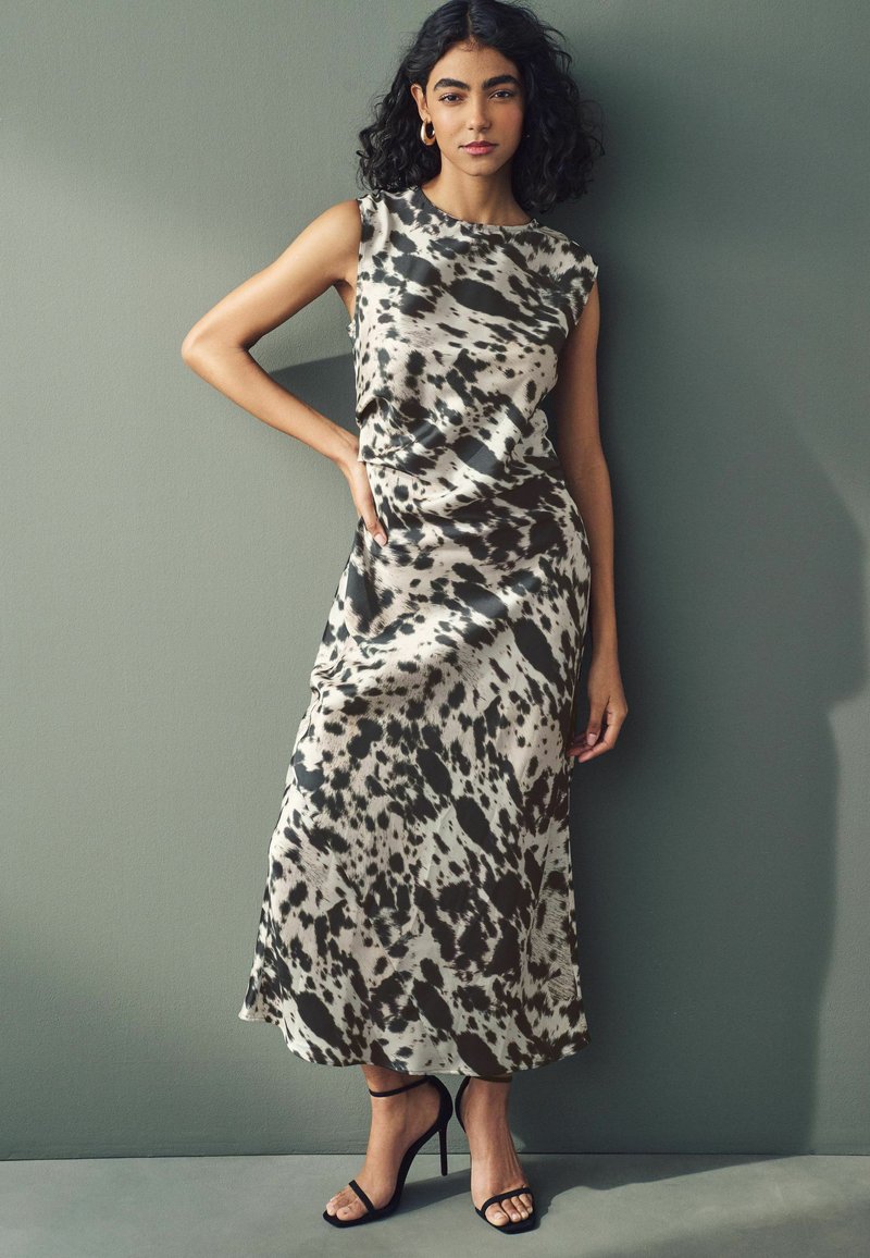 Midi dress in a beige and black abstract print, sleeveless design, smooth fabric, paired with black strappy heels.
