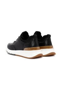 Zwarte sportieve sneakers met een gladde leren afwerking, voorzien van een witte tussenzool en een tan accent op de hiel, ontworpen voor comfort en duurzaamheid.