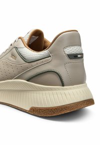 Sneaker in pelle beige con accenti testurizzati, pannelli in rete e suola in gomma marrone chiaro. Presenta il nome del brand sul lato e sul tallone.