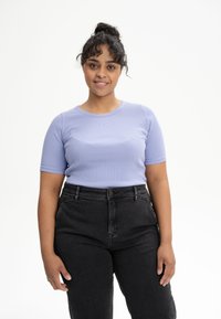 Lichtpaarse geribde t-shirt met korte mouwen, ronde halslijn, gecombineerd met hoge zwarte jeans. Model staat voor een effen witte achtergrond.