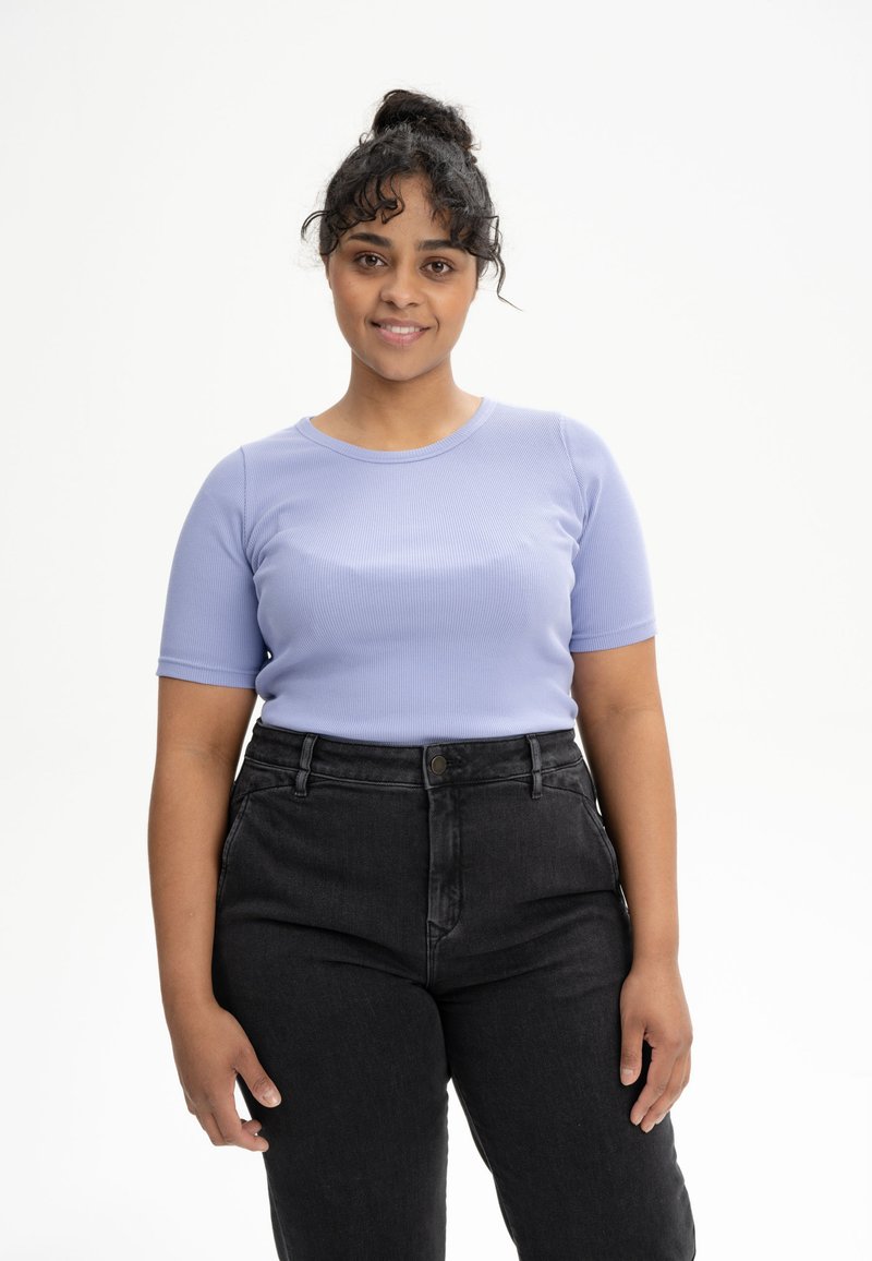 Lichtpaarse geribde t-shirt met korte mouwen, ronde halslijn, gecombineerd met hoge zwarte jeans. Model staat voor een effen witte achtergrond.