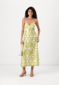 Vestido maxi em verde e branco vibrantes com um padrão em espiral, apresentando alças finas e um decote em V. Tecido suave com um design fluido.