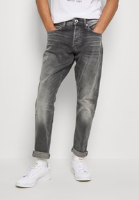 Grå denimjeans med en blekt finish, avslappnad passform, uppvikta muddar och femfickorsdesign, i kombination med vita sneakers.