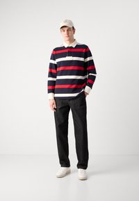 Stribet langærmet polo i navy, rød og hvid, har en krave og en brystlomme. Samlet med mørke denim jeans og hvide sneakers.